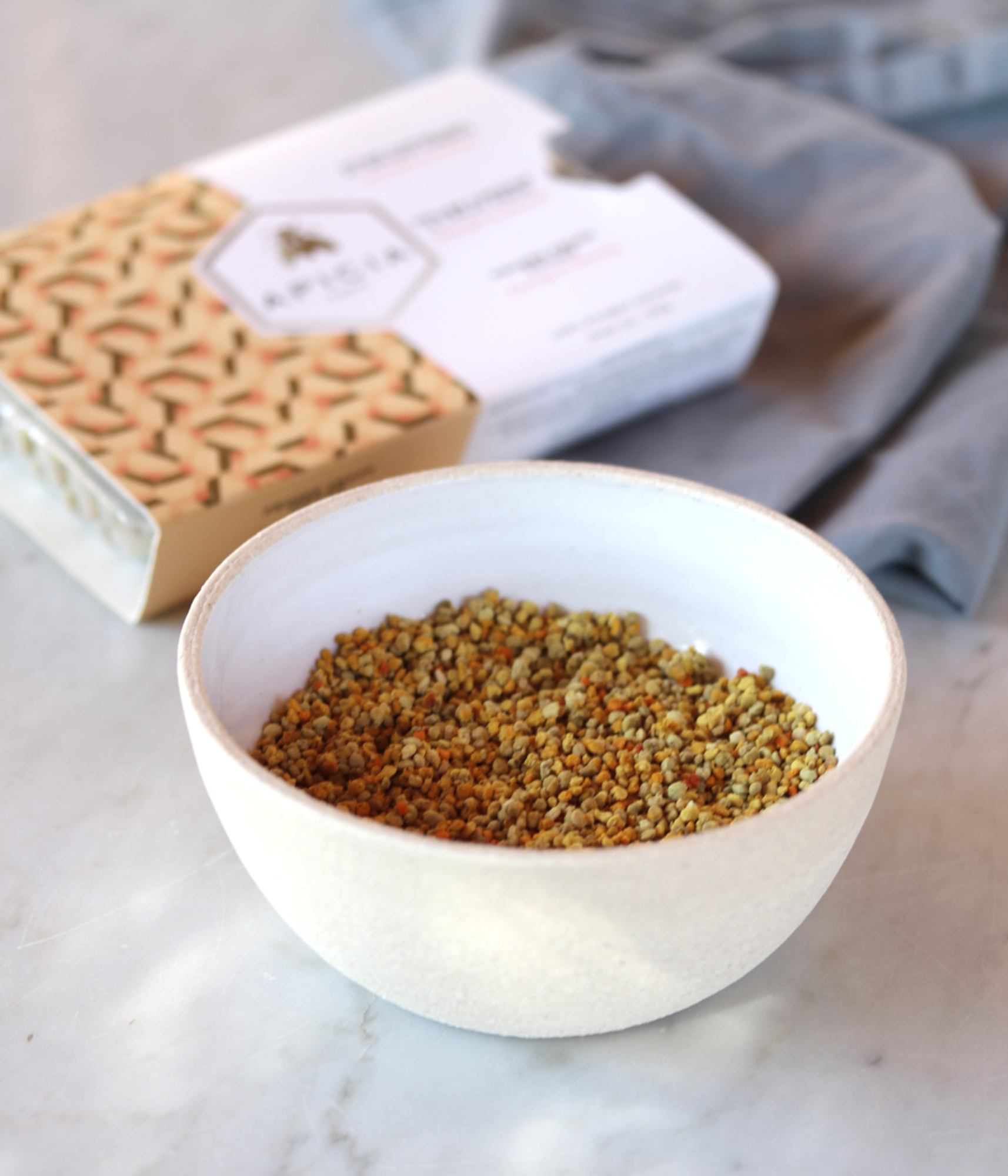 Bol en céramique de pollen frais avec une boîte de pollen frais en arrière-plan, sur une table en marbre blanc.