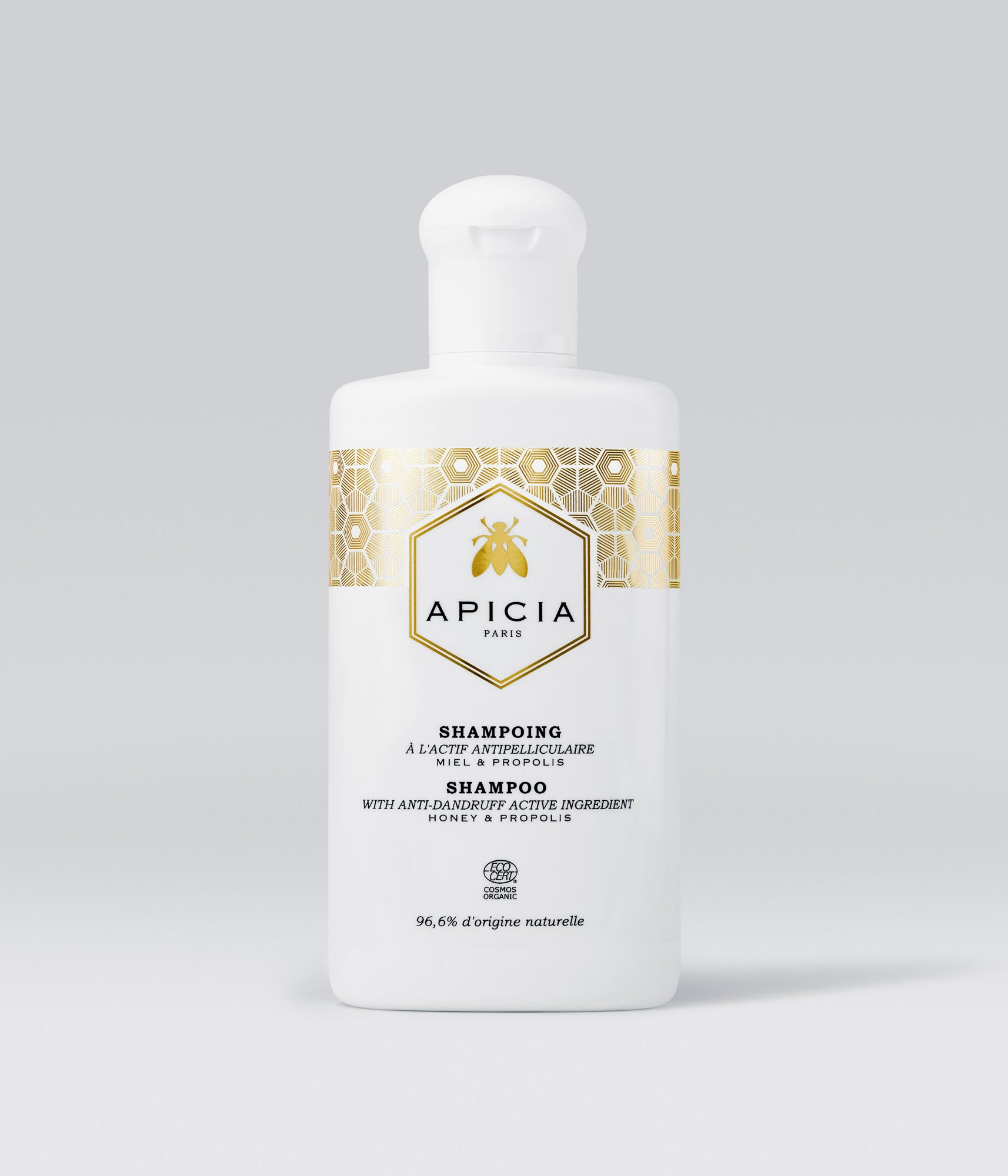 Packshot d'une bouteille de shampoing blanche et dorée sur un fond gris.