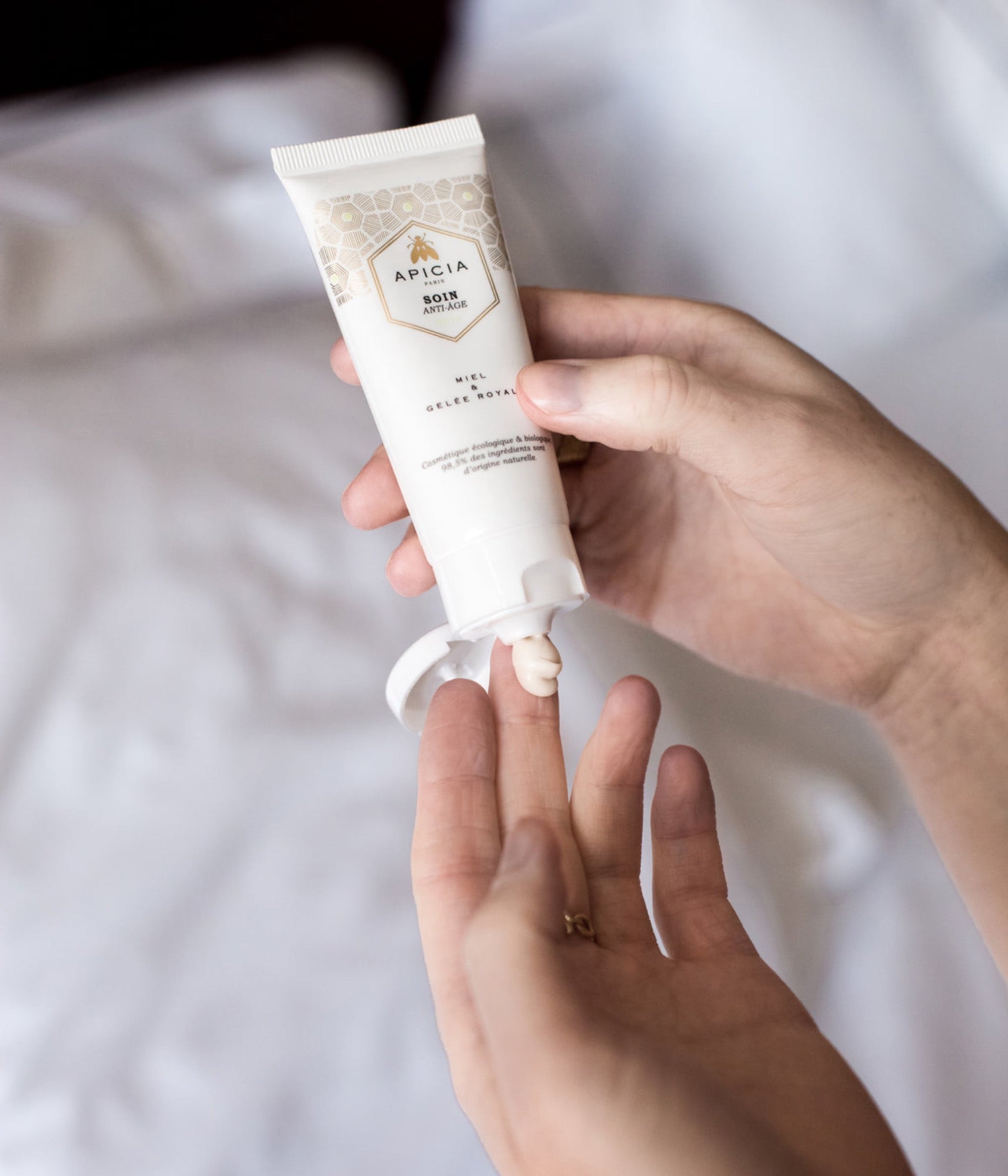 Une main pressant de la crème blanche depuis le contenu d'un tube blanc sur les doigts de l'autre main.