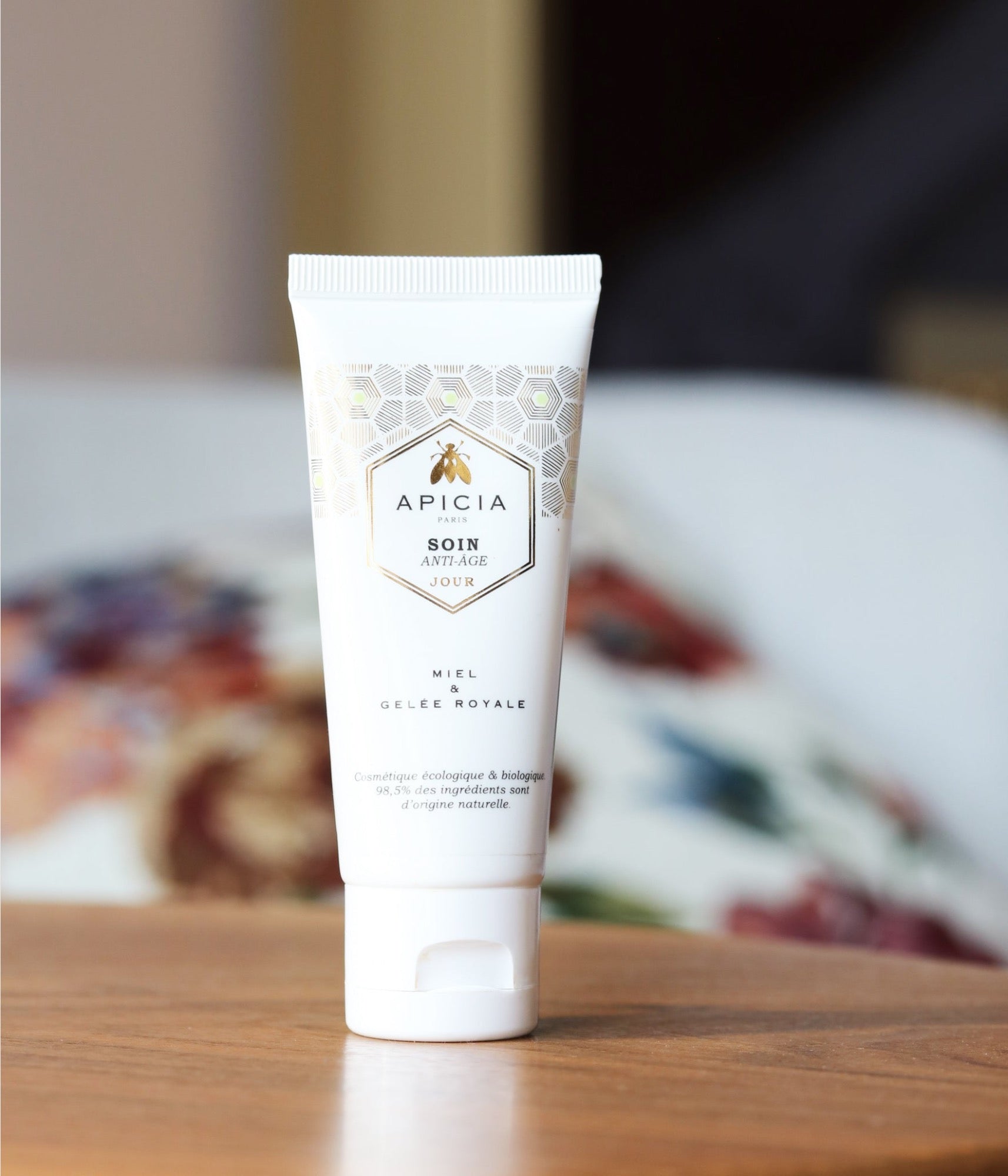 Un flacon de crème pour le visage blanc et doré sur une table de nuit en bois.