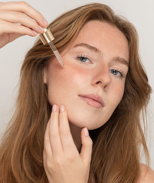 Girl holding to her check bone a dropper of clear liquid