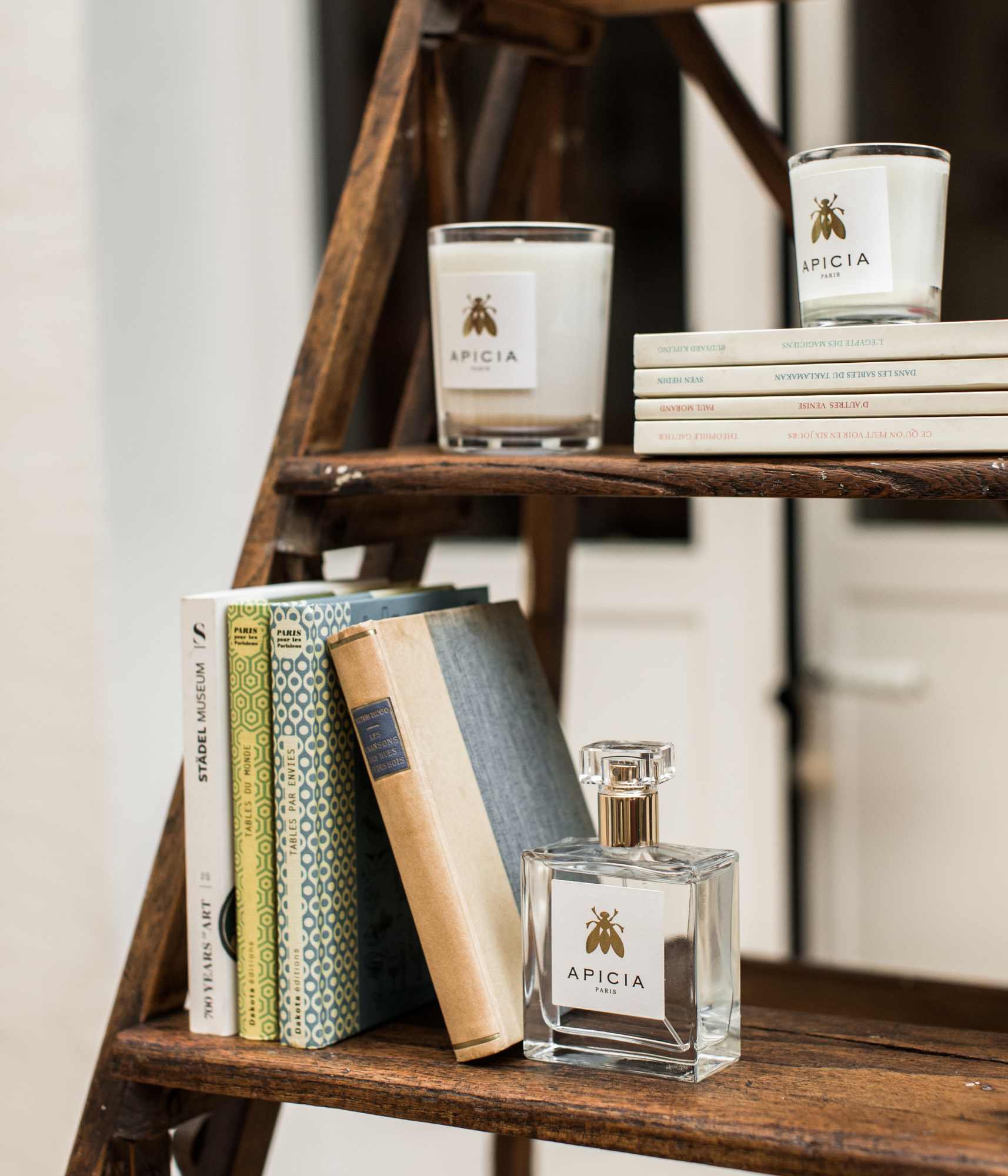 Étagère en bois avec des livres de différentes couleurs, deux bougies blanches et un flacon de parfum d'intérieur en verre.