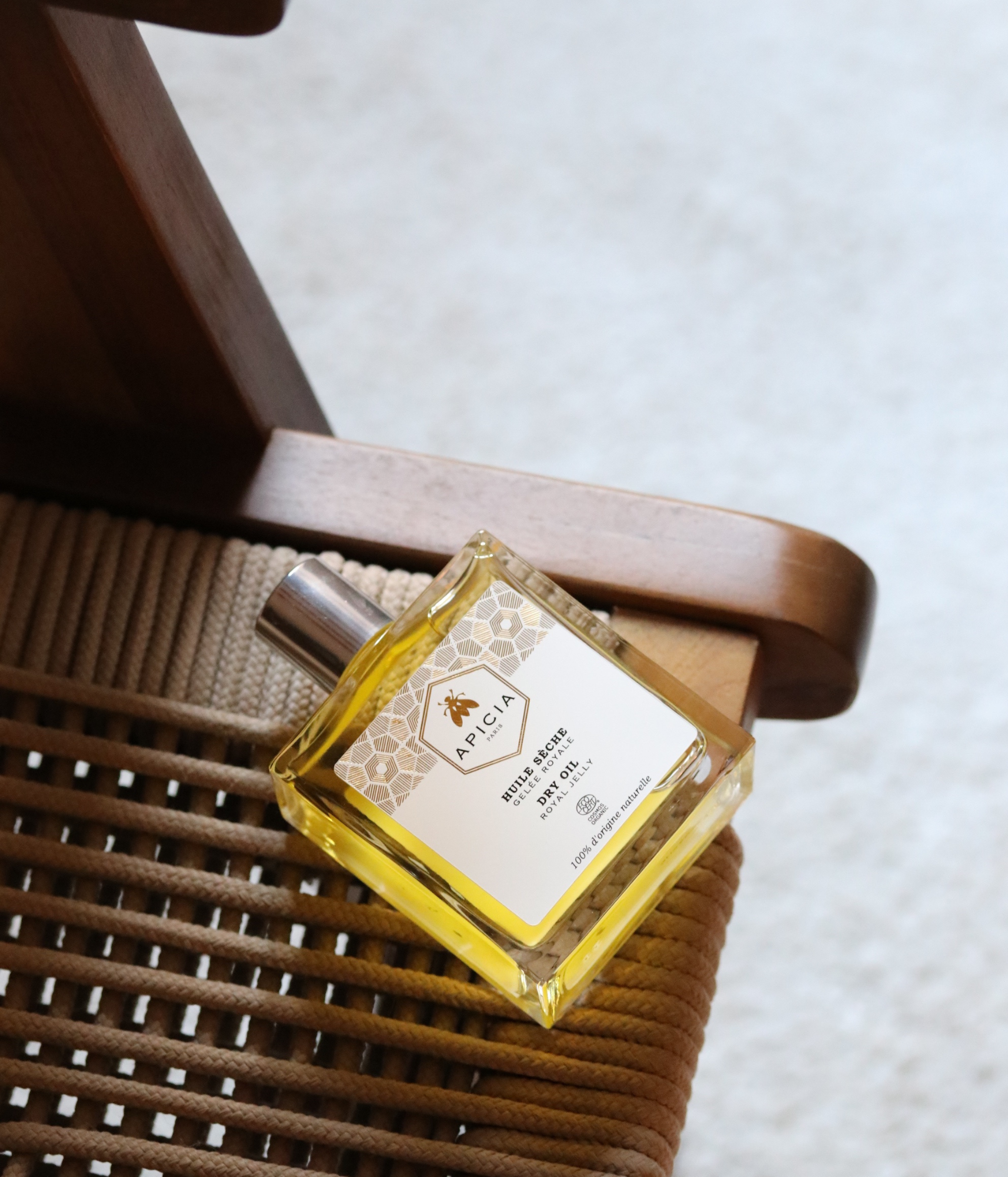 Un flacon rectangulaire en verre transparent, contenant de l’huile, repose sur le bord d'une chaise en bois.