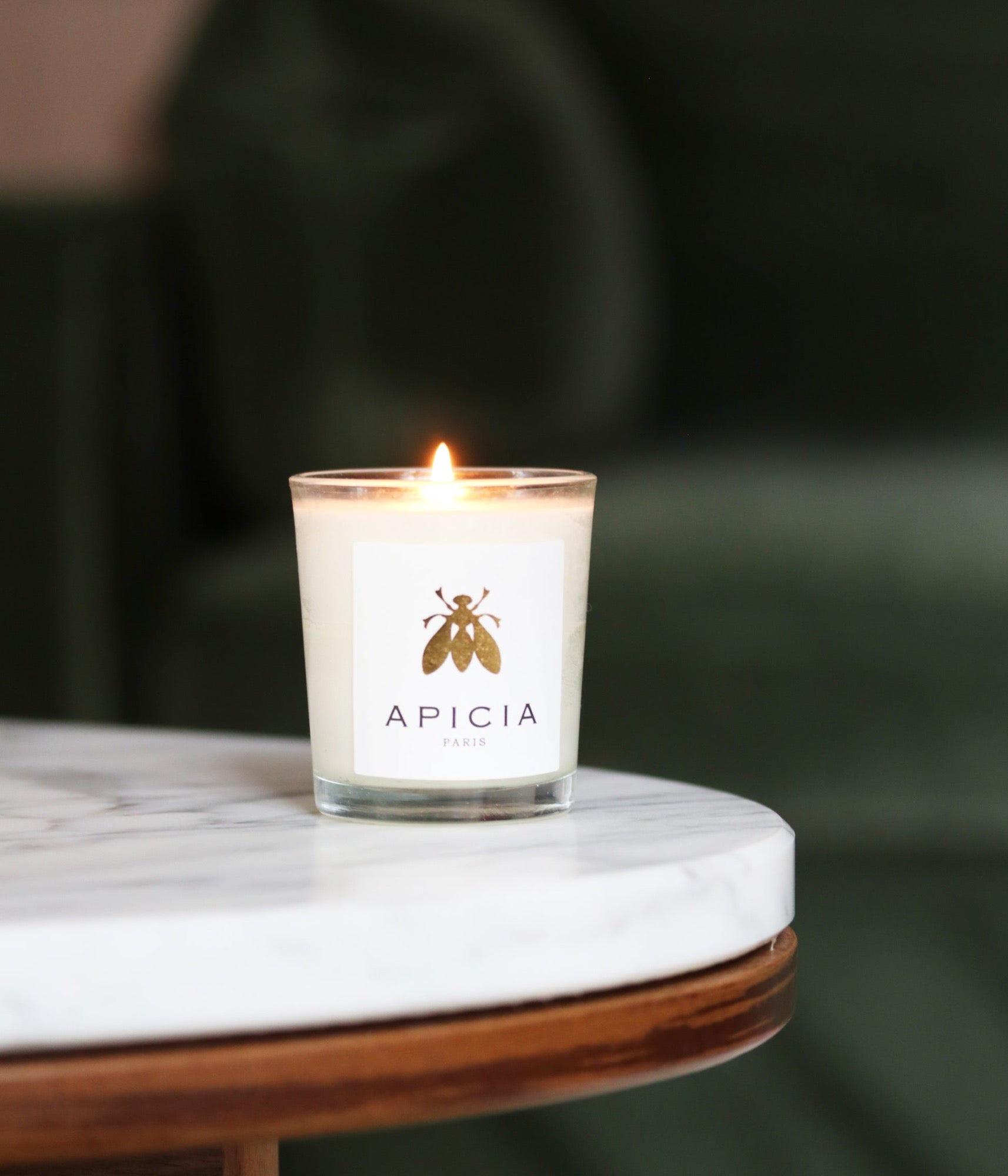 Bougie blanche dans un verre transparent posée sur une table en marble blanc avec un fond vert foncé.