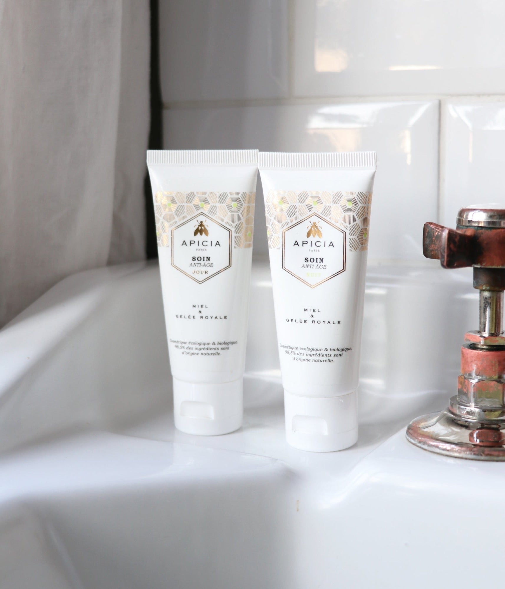 Deux tubes de crème visage blancs et dorés sur le rebord d'un lavabo blanc.